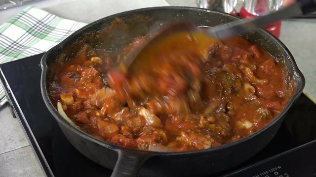 Stirring spaghetti sauce with meat in a cast iron skillet
