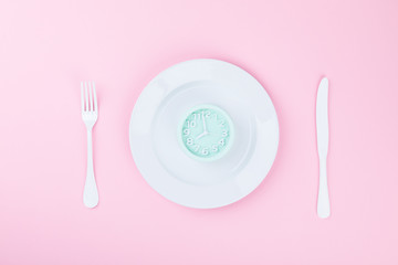 Concept minimal "Time to Eat". Alarm Clock on a white Plate on a pink pastel Background. Top View. Flat Lay. Copy space for Text.