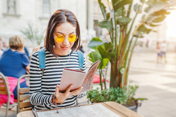 Young beautiful traveler woman in reading the menu and making an order at the terrace of cafe,...