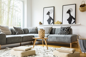 Poufs on carpet in bright african living room interior with grey corner sofa and posters. Real photo