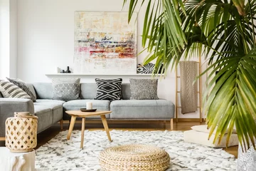 Tapeten Pouf and wooden table in modern living room with painting above grey corner couch. Real photo © Photographee.eu
