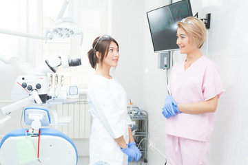 Fototapeta premium Two young girls-dentists in the treatment room. Look at each other and smile