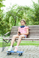 Girl  with her skateboarrd in the park sitting down on  a bench 