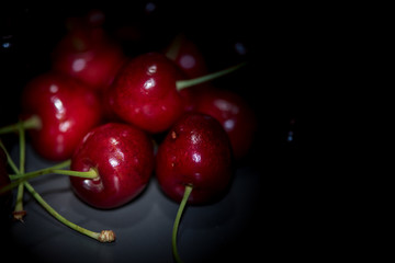 Dark, ripe and juicy cherries on a black plate