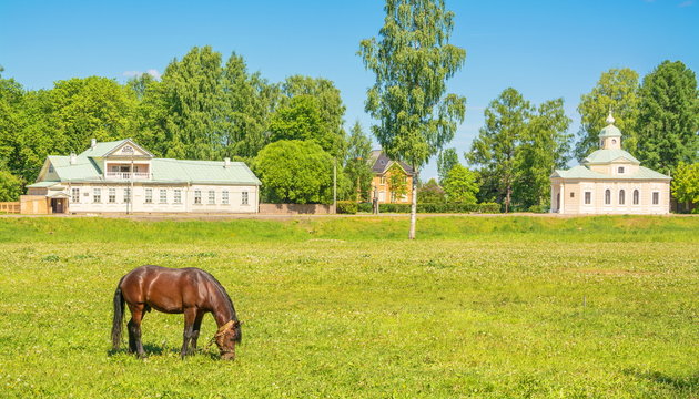 Rural landscape with a horse on the background of an ancient chapel and a beautiful wooden mansion