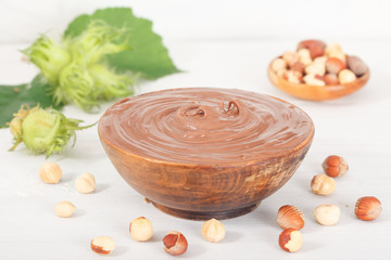 Sweet chocolate hazelnut spread with whole nuts and green hazelnut on white table. Nutella cream.