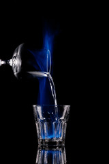 close up view of pouring burning sambuca alcohol drink into glass process on black background