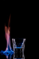 close up view of glass of burning sambuca drink on black background