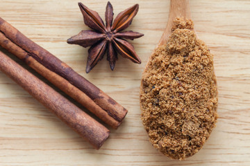 Top view natural brown sugar or unrefined sugar on wood spoon and cinnamon stick and anise on wooden table with copy space. Sweet seasoning for good health. Ingredient prepared for cooking or bakery..