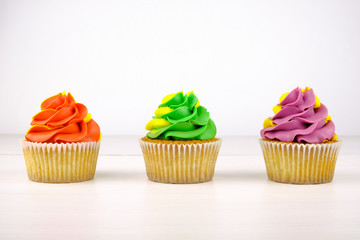 Three cupcakes with colorful cream on white wooden table.