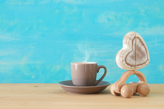 Image of hot coffee or tea next to toy car with heart over wooden table. Father's day concept.