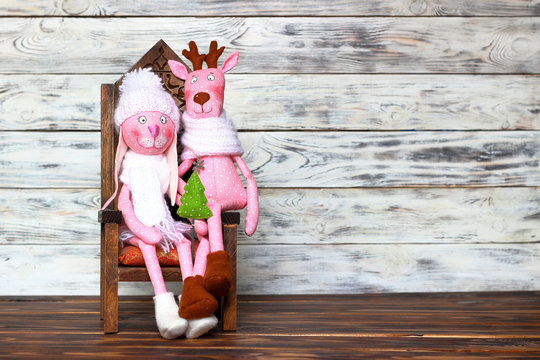 Doll-toy of a pink rabbit girl in a white hat with a green fir-tree and deer sitting on a chair. Love, romantic and friendship. Concept of joy and winter holidays