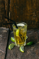 Delicious alcoholic cocktail with lemon and lime, pieces of ice on a wooden background