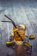 Delicious alcoholic cocktail with lemon and lime, pieces of ice on a wooden background