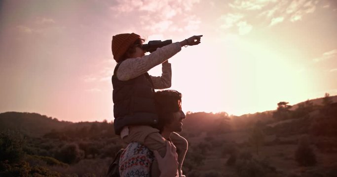 Boy on hiker father's shoulders using binoculars for bird watching