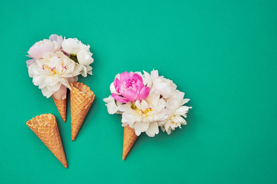 Ice cream cones with white peony flowers on green background. Summer concept. Copy space, top view
