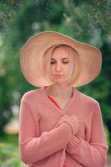 Portrait of beautiful young woman in wide beach hat, against background of summer green park