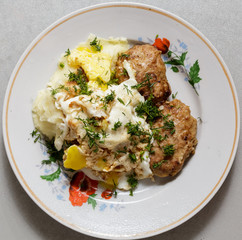 Mashed potatoes, eggs and cutlets lie on a round plate.