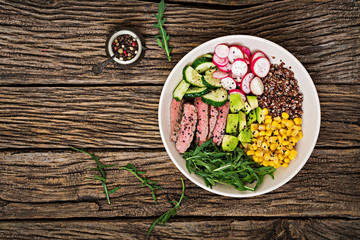 Healthy dinner. Buddha bowl lunch with grilled beef steak and quinoa, corn, avocado, cucumber and arugula on wooden background. Meat salad. Flat lay. Top view