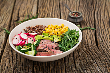 Healthy dinner. Buddha bowl lunch with grilled beef steak and quinoa, corn, avocado, cucumber and arugula on wooden background. Meat salad.