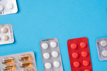 Different tablets and pills in the package and without it on a blue background