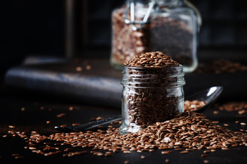 Flax or linen seeds in jar on brown stone background, selective focus