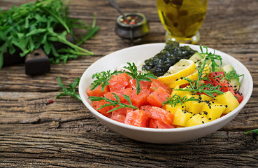 Hawaiian salmon fish poke bowl with rice, avocado, mango, tomato, sesame seeds and seaweeds. Buddha bowl. Diet food.