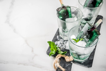 Trendy food, Asian vegan desserts, homemade ice cream popsicles with algae spirulina, served with mint in glasses with ice, white marble background copy space