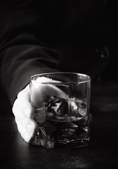 Glass with whiskey in hand, dark background, selective focus