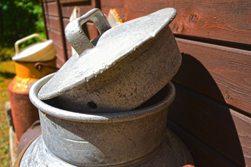 Two old milk churns on the wooden wall of a shed in bright sunlight