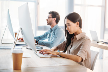 side view of focused interracial business colleagues working at workplace in office