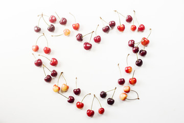 Yellow and dark red cherries on white are lined in the shape of heart. Summer and love concept. Top view, flat lay