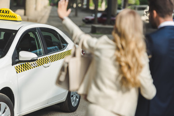 selective focus of young woman waving hand while going with man to taxi