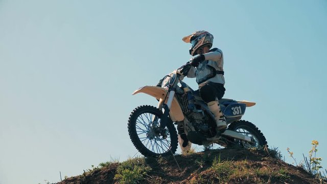 Motocross participant with his motorbike on a hillock