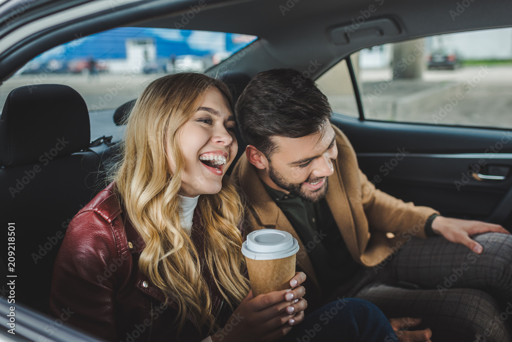 Wall mural happy young couple laughing while sitting together in taxi