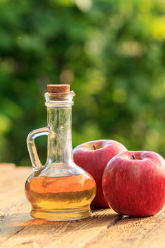 Apple vinegar in glass bottle with cork and fresh red apples on old wooden boards with blurred green natural background. Organic food for health