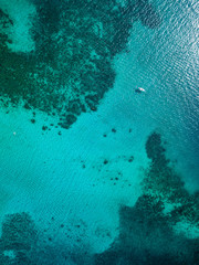 Top down aerial drown view of a small boat over a tropical coral reef in a clear ocean