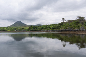 Beautiful beach, with mountains in the background and cloudy skies, with forest along the coast. Taken in Letterfrack along the Wild Atlantic Way, Ireland in summer.
