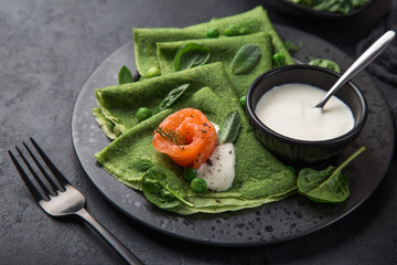 spinach crepes with smoked salmon and yogurt sauce on black plate