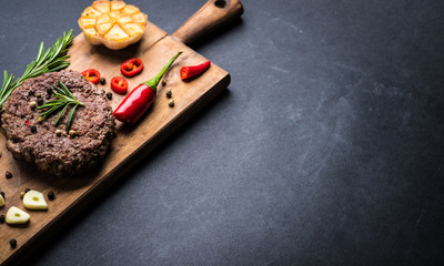 Homeemade beef burger cutlet with herbs and spices on wooden cooking board. Space for text