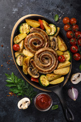 grilled spiral sausages and vegetables on dark plate
