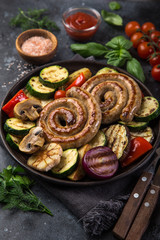 grilled spiral sausages and vegetables on dark plate