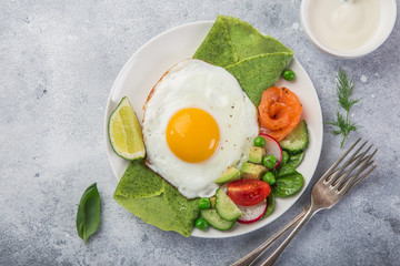green spinach crepes with fried eggs, smoked salmon and vegetables for breakfast