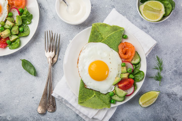 green spinach crepes with fried eggs, smoked salmon and vegetables for breakfast