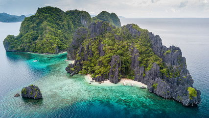 Aerial drone view of a tiny tropical island with beach, coral reef and sharp limestone cliffs (Shimizu Island, El Nido)