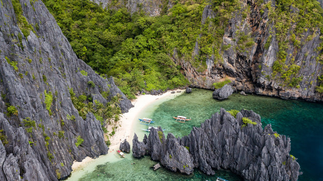 Aerial drone view of a small, quiet tropical beach in a small bay surrounded by huge limestone cliffs (Shimizu Island)