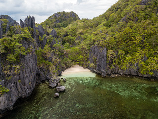 Fototapeta na wymiar Aerial drone view of boats around a tiny sandy beach on a tropical island surrounded by towering limestone cliffs
