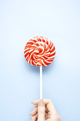 Sweet holiday / Creative concept photo of hand holding lollipop candy on blue background.