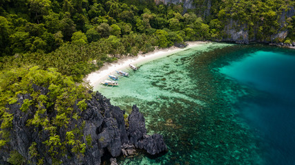 Aerial drone view of a small, tropical sandy beach and tourist boats over a coral reef