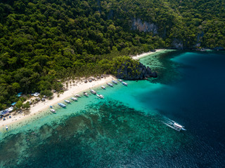 Fototapeta na wymiar Aerial drone view of traditional Banca boats and coral reef surrounding a scenic tropical sandy beach (7 Commando Beach, El Nido)